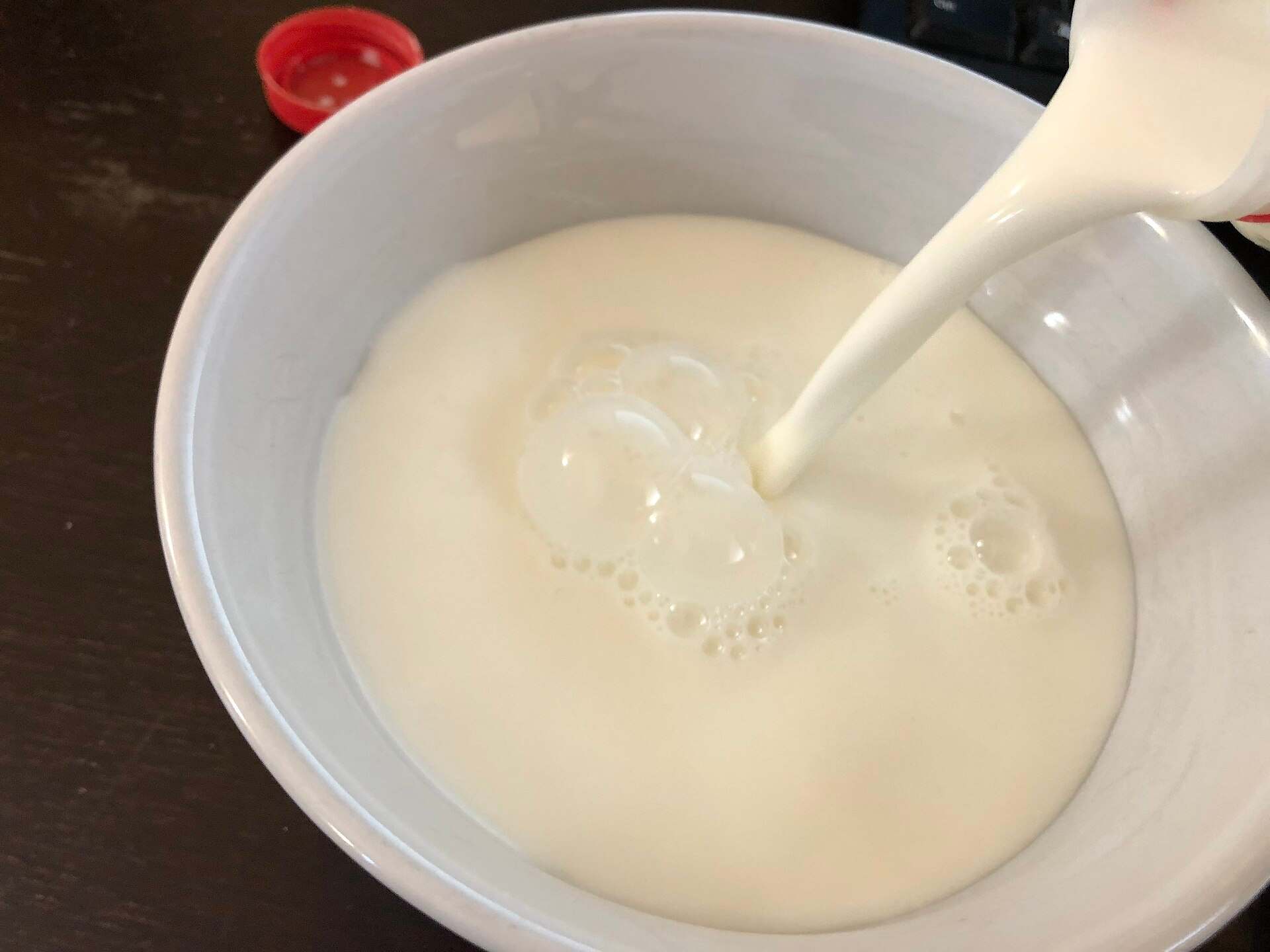 Fresh milk being poured into a ceramic bowl from above — overhead view