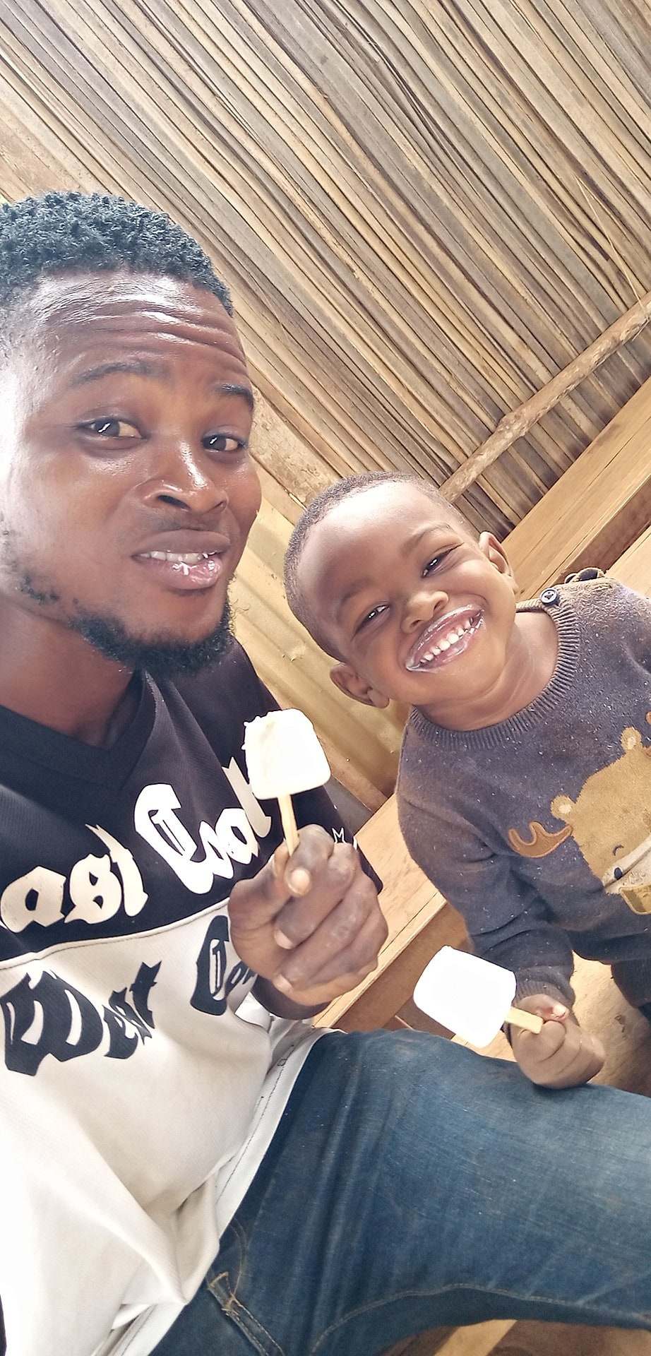 A father and his young son both smiling broadly while eating yoghurt